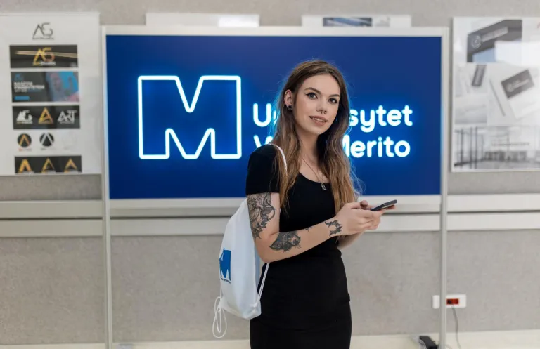 Rankingi i akredytacje | Uniwersytet WSB Merito Bydgoszcz: studentka z telefonem w ręku na korytarzu uczelni