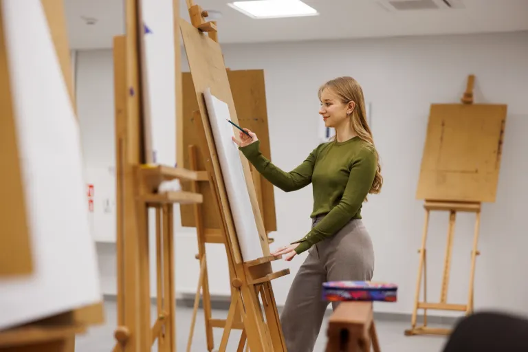 Plenerowa wystawa studentów kierunku design w biznesie: 20-lecie Uniwersytetu WSB Merito Bydgoszcz w roku 680. urodzin Miasta Bydgoszczy | Aktualności | Uniwersytet WSB Merito Bydgoszcz: studentka rysująca przy sztaludze