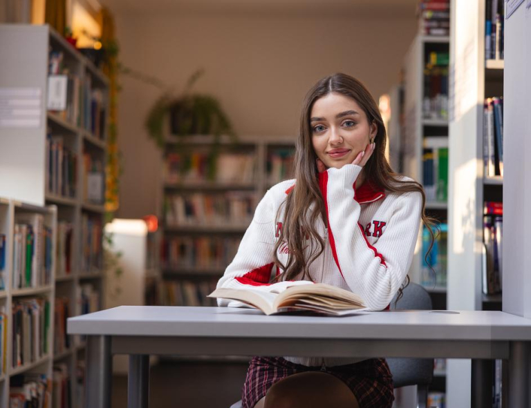 Biblioteka | Uniwersytet WSB Merito Chorzów: Studentka czytająca książkę w bibliotece