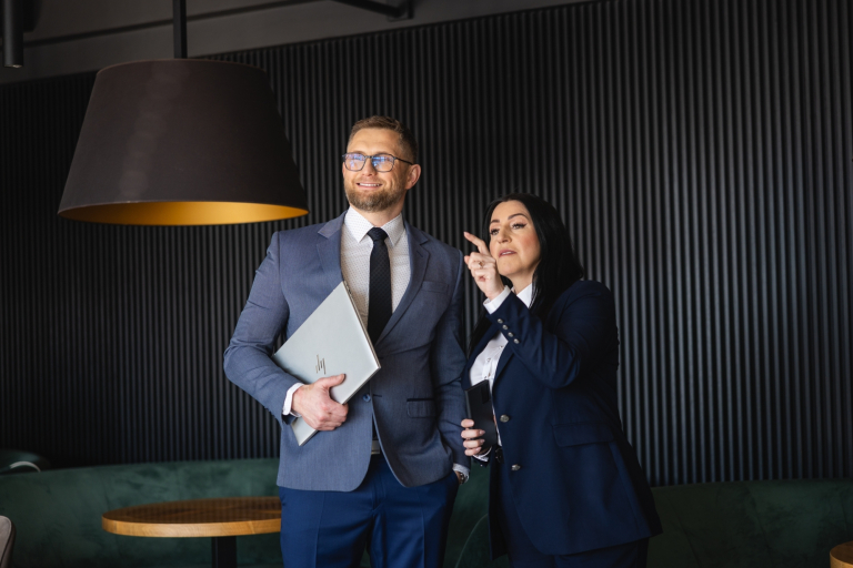 Organizacja studiów | Uniwersytet WSB Merito Chorzów: Uczestnicy MBA kobieta i mężczyzna stoją na korytarzu z laptopem i telefonem- Uniwersytet WSB Merito Chorzów