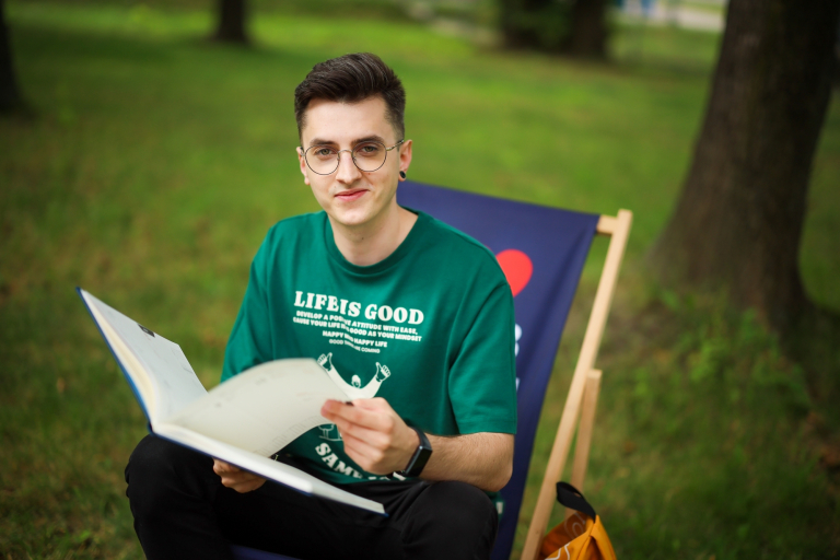 Strefa studenta | Uniwersytet WSB Merito Chorzów: Student WSB MErito siedzi na leżaku w parku i przegląda notatnik