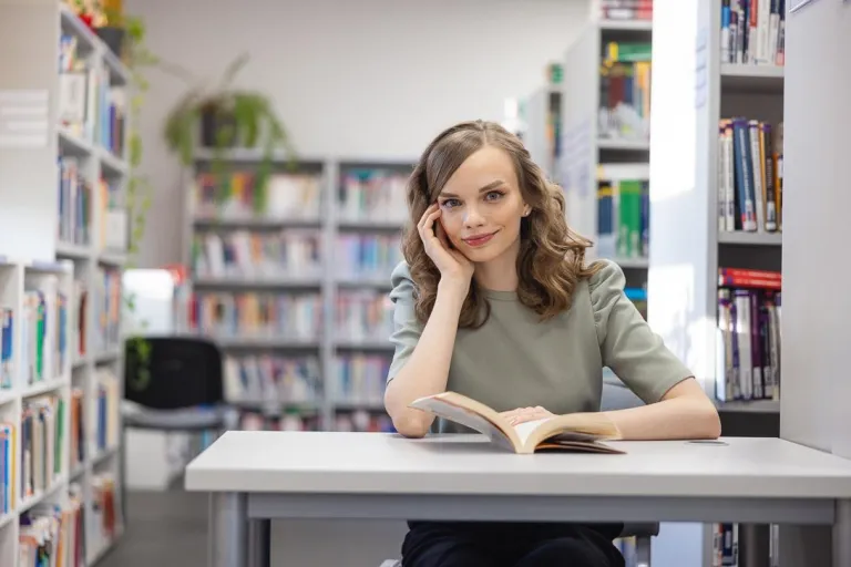 Pracownik służby cywilnej | Studia I stopnia w Chorzowie | Uniwersytet WSB Merito Chorzów: studentka siedząca i czytająca książkę w bibliotece