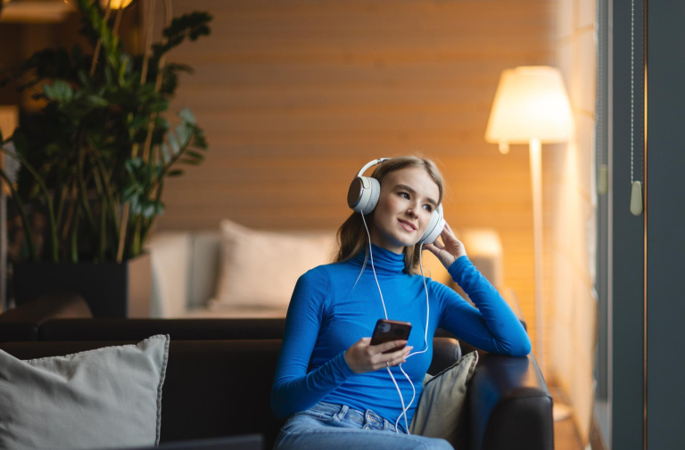 Our campus | WSB Merito Bydgoszcz University: studentka ze słuchawkami na uszach siedzi na sofie i patrzy w skupieniu za okno