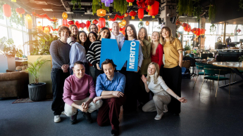 International Business Management, studia II stopnia, magisterskie: Zdjęcie grupowe studentów w industrialnej przestrzeni. Po środku trzymają sygnet logo Uczelni Merito