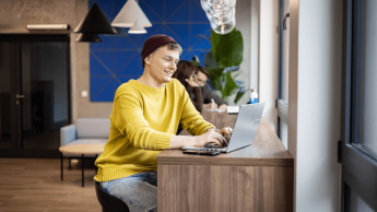 Digital Marketing, studia II stopnia, magisterskie: Student siedzi przy laptopie, ma na sobie żółty sweter i fioletową czapkę