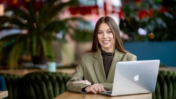 Management | WSB Merito Gdańsk University: Studentka ubrana w oliwkową marynarkę siedzi w kawiarni przy laptopie