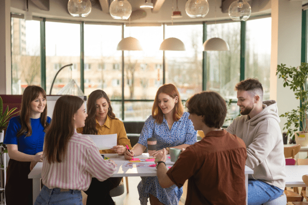IACBE Accreditation | WSB Merito Gdańsk University: Grupa studentów siedzi przy stole i pracuje nad projektem. Wokół jest oszklona przestrzeń, do środka wpada dużo światła. 