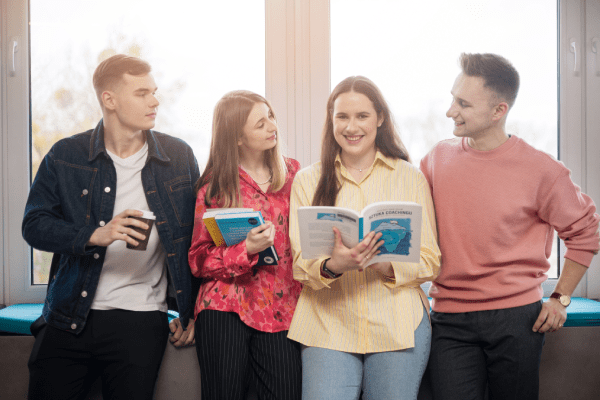 Who we are | WSB Merito Gdańsk University: Studenci - dwie dziewczyny i dwóch chłopaków - stoją pod oknem w świetle 