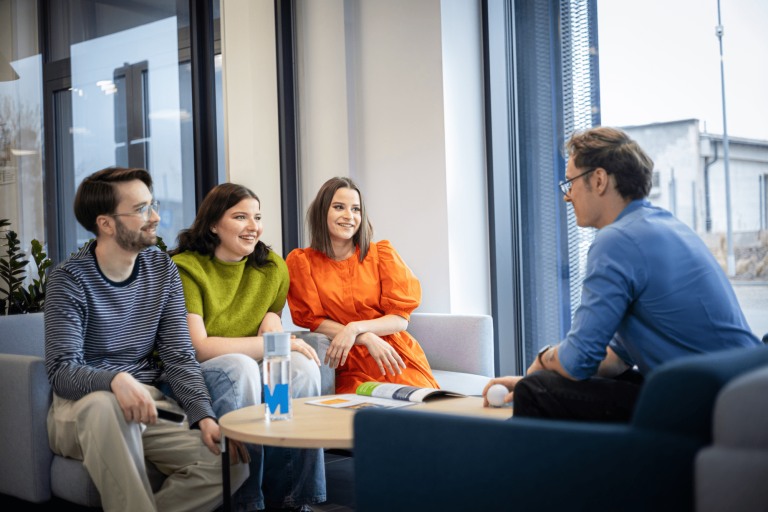 Our campus | WSB Merito Gdańsk University: Studenci siedzą w holu i rozmawiają siedząc na kanapach