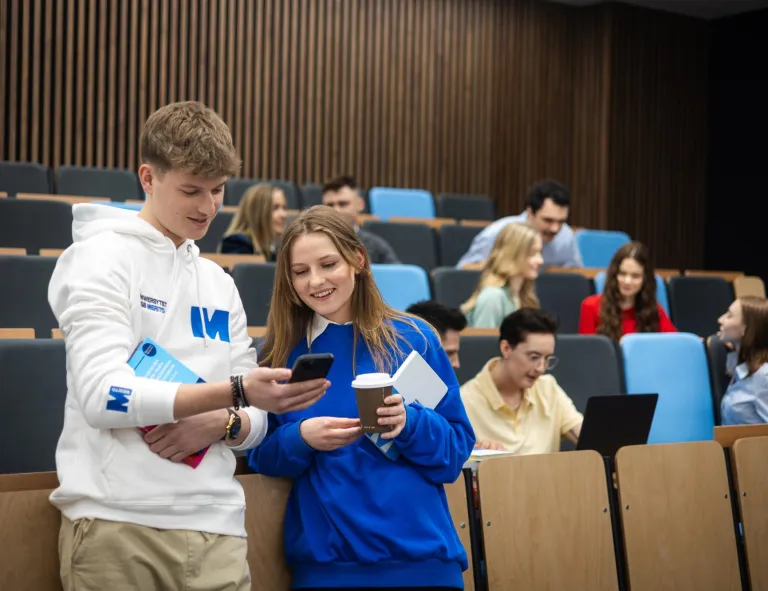 Bachelor's degree | WSB Merito Gdańsk University: Studenci w auli, chłopak i dziewczyna pokazują sobie coś na komórce