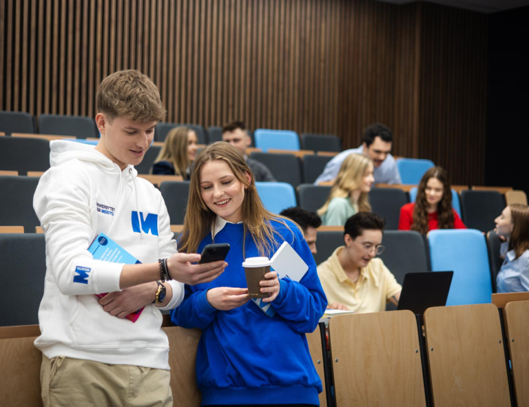 Bachelor's degree | WSB Merito Gdańsk University: Studenci w auli, chłopak i dziewczyna pokazują sobie coś na komórce