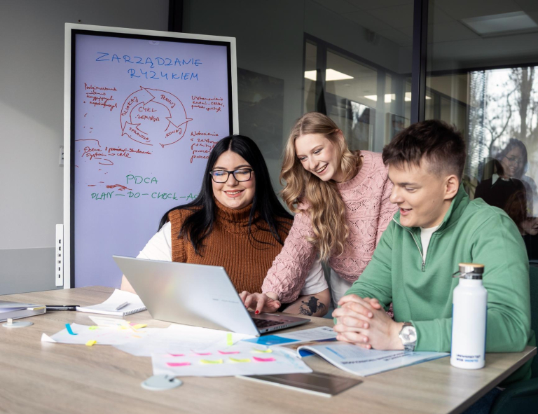 Management, studia I stopnia, licencjackie i inżynierskie: Studenci w bibliotece siedzą przy biurku i opracowują jakieś zagadnienie przy laptopie