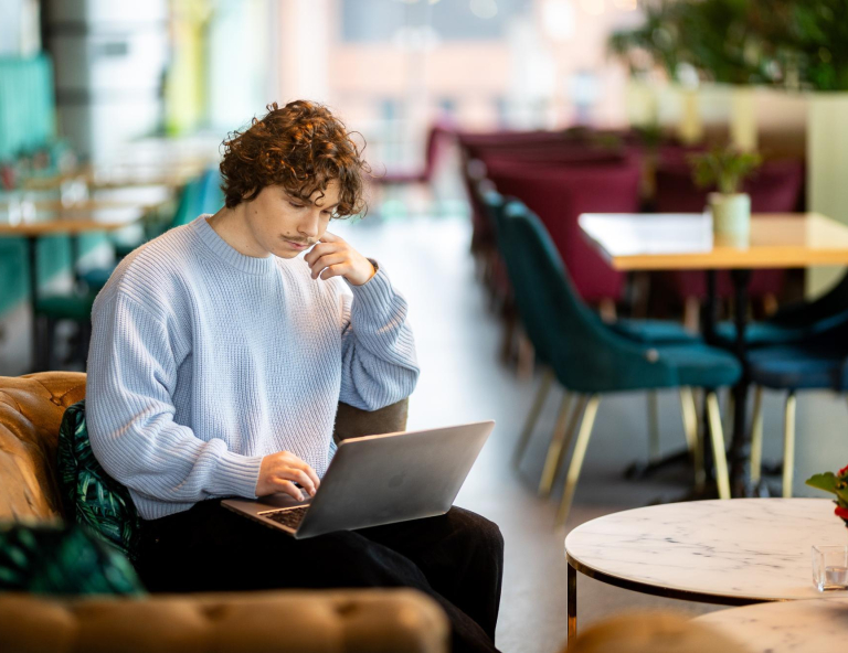 Software Development, studia I stopnia, licencjackie i inżynierskie: Student siedzi na kanapie w kawiarni i pracuje na laptopie