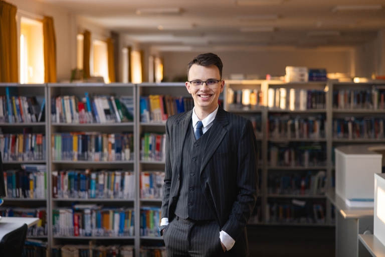 International Business, studia I stopnia, licencjackie i inżynierskie: Student w bibliotece ubrany w garnitur 