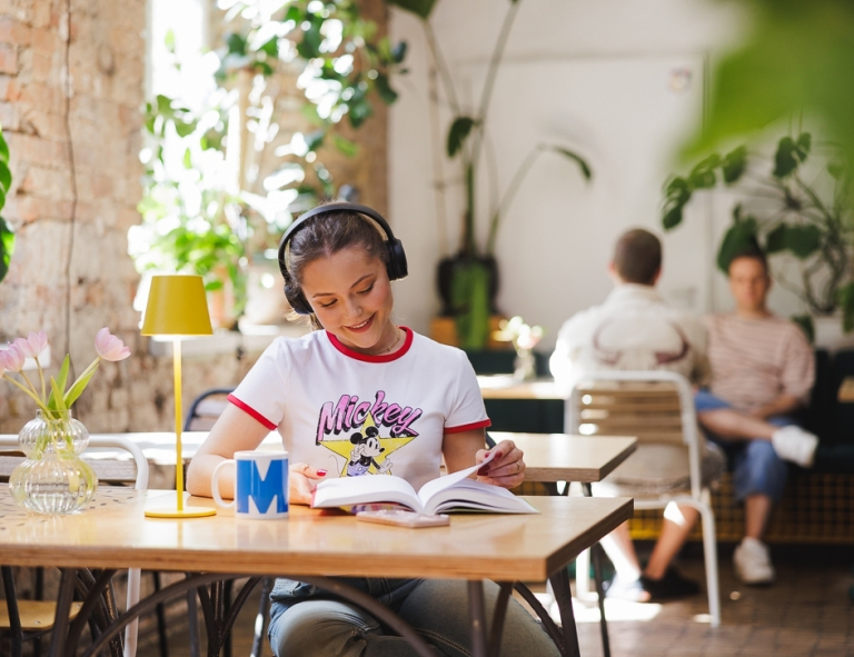 Student Council | WSB Merito Gdańsk University: Studentka siedzi w strefie studenta pijąc kawę w kubku z logo WSB Merito i słucha muzyki