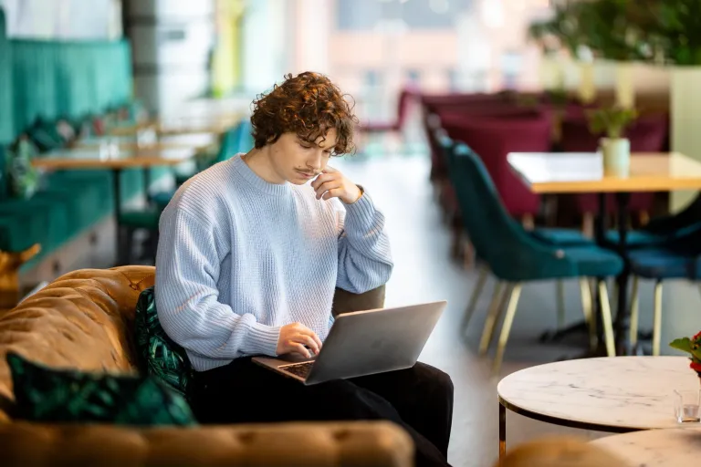 Management | WSB Merito Gdańsk University: Student siedzi na kanapie w kawiarni i pracuje na laptopie