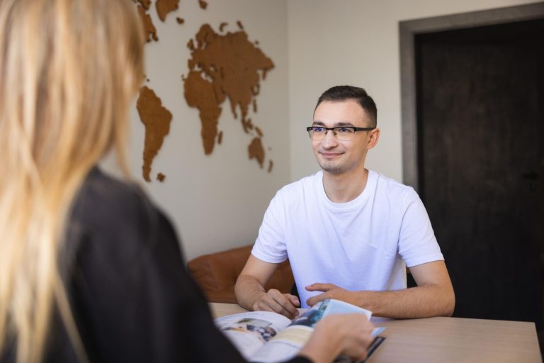 Bachelor's degree | WSB Merito Łódź University: Mężczyzna w białej koszulce siedzi przy stole, uśmiechając się do kobiety z książką.