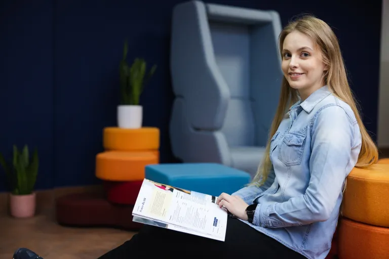 Student ABC | WSB Merito Łódź University: Grafika główna: WSB Merito Łódź, dla nowych studentów, studentka siedzi na sofie i przegląda informator uniwersytetu