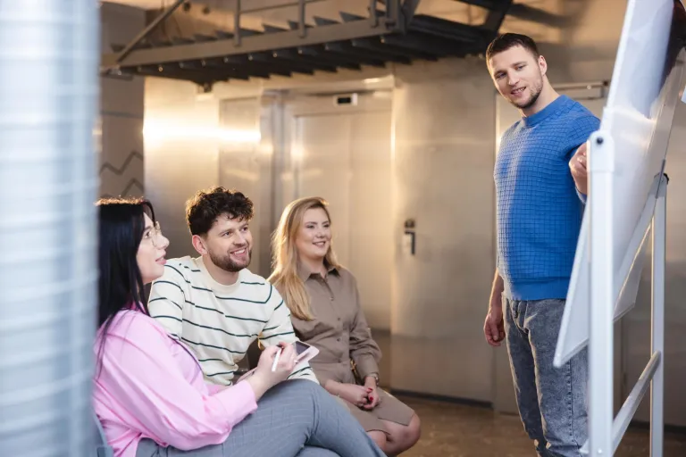 Management | WSB Merito Łódź University: Student prezentuje na tablicy, a trójka słucha.