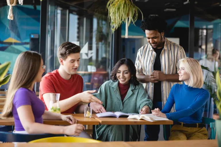 International Business | WSB Merito Łódź University: Piątka studentów siedzi przy stole i dyskutuje nad książką.