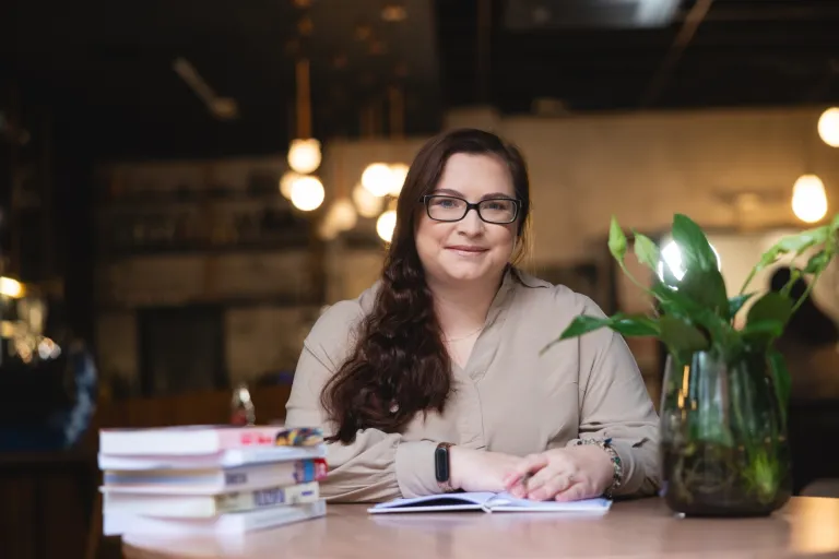 Our values | WSB Merito Opole University: Główna grafika: Opole - studentka siedząca w kawiarni, obok stos książek