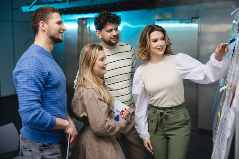 Digital university | WSB Merito Opole University: Studenci oglądający notatki przypięte na dużej tablicy