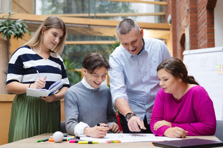 Our values | WSB Merito Opole University: Grupa 3 studentów pracuje razem z wykładowcą przy stole