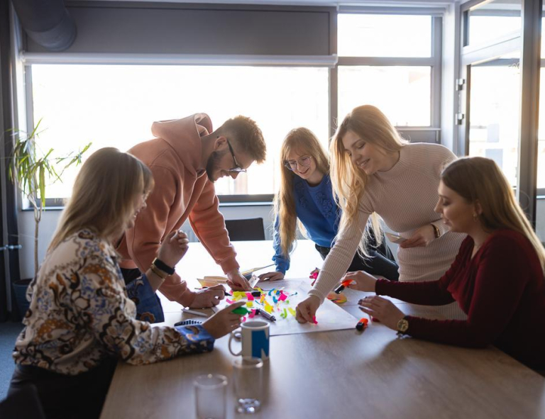 Social impact | Uniwersytet WSB Merito Szczecin: Grupa studentów wspólnie pracuje nad kreatywnym projektem, używając kolorowych karteczek i markerów.