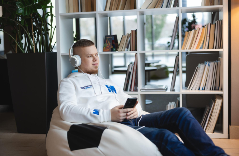 Digital university | WSB Merito Toruń University: student ze słuchawkami na uszach i telefonem w ręku siedzi na pufie