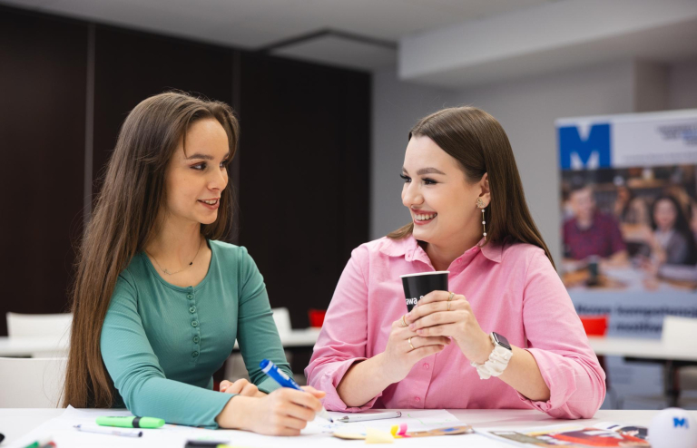 Our values | WSB Merito Toruń University: dwie uśmiechnięte studentki siedzą przy stole i rozłożonych notatkach