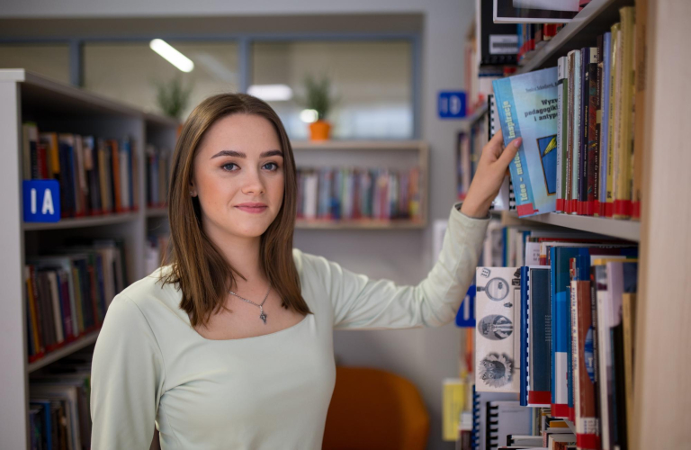 Library | WSB Merito Toruń University: studentka w bibliotece przy regale z książkami