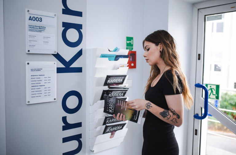 Career Office | WSB Merito Toruń University: studentka przed gabinetem biura karier, przegląda magazyn