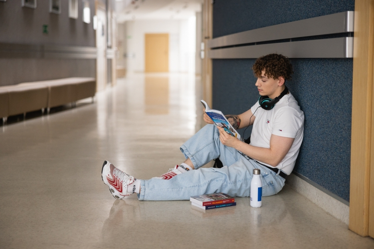 Who we are | WSB Merito Toruń University: Główna grafika: Toruń - studia I stopnia - student siedzący na korytarzu