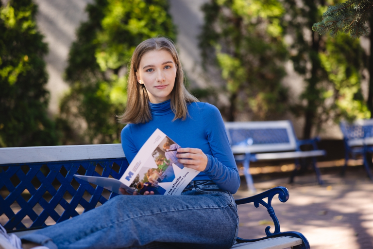 Student ABC | WSB Merito Warsaw University: Grafika główna: WSB Merito Warszawa, dla nowych studentów, studentka w niebieskim sweterku siedzi na ławce w plenerze i przegląda informator uniwersytetu