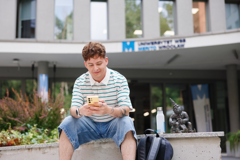 Our campus | WSB Merito Wrocław University: is "a student sitting next to a gnome in front of the campus building