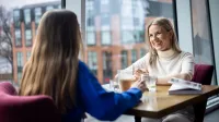Efektywność energetyczna, odnawialne źródła energii i inne narzędzia prowadzące do transformacji energetycznej | Uniwersytet WSB Merito w Gdańsku: Studentki rozmawiają podczas wizyty w kawiarni. Siedzą przy stoliku przy kawie