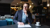 Inżynieria oprogramowania w JavaScript (TypeScript) | Studia podyplomowe w Gdańsku | Uniwersytet WSB Merito w Gdańsku: Mężczyzna w ubraniu biznesowym siedzi przy biurku z filiżanką kawy