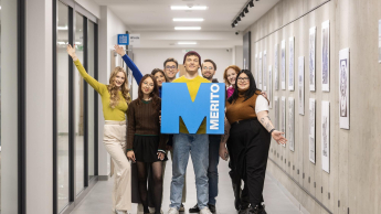 Kreowanie treści w mediach cyfrowych | Studia II stopnia ze studiami podyplomowymi  | Uniwersytet WSB Merito w Gdańsku: Zdjęcie grupowe studentów na korytarzu z sygnetem "M"