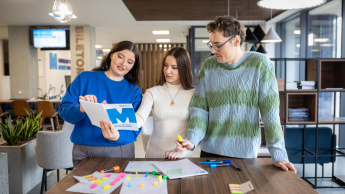Kontynuuj studia | Uniwersytet WSB Merito w Gdańsku: Dwie studentki i student stoją nad stołem i wykonują zadanie