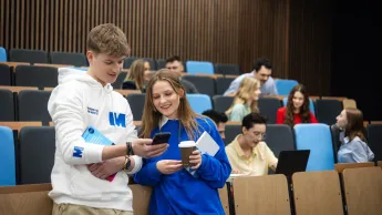 Pedagogika opiekuńczo-wychowawcza z proﬁlaktyką społeczną | Uniwersytet WSB Merito w Gdańsku: Studenci w auli, chłopak i dziewczyna pokazują sobie coś na komórce