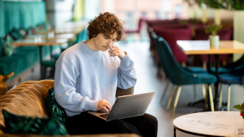 Front-end Developer | Studia I stopnia w Gdańsku | Uniwersytet WSB Merito w Gdańsku: Student siedzi na kanapie w kawiarni i pracuje na laptopie