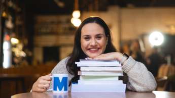 Social media i influencer marketing | Uniwersytet WSB Merito w Gdańsku: Portret kobiety, która opiera się brodą o książki, uśmiecha się