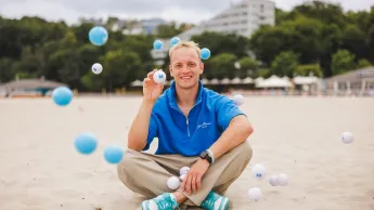 Menedżer sprzedaży | Studia I stopnia w Gdańsku | Uniwersytet WSB Merito w Gdańsku: Student siedzi po turecku na plaży, wokół niego latają piłeczki
