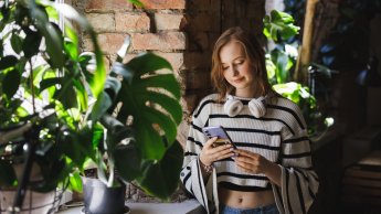 Studentka z komórką stoi przy oknie przy zielonym parapecie