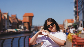 Menedżer turystyki i hotelarstwa | Studia I stopnia w Gdańsku | Uniwersytet WSB Merito w Gdańsku: Studentka pokazuje znak serca będąc niedaleko Żurawia w Gdańsku