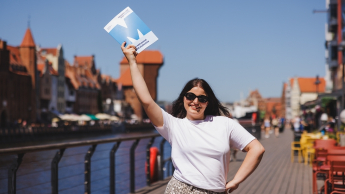 Finanse przedsiębiorstw i podatki z certyfikatem ACCA | Studia II stopnia ze studiami podyplomowymi  | Uniwersytet WSB Merito w Gdańsku: Studentka z teczką z sygnetem M, z tyłu widać Gdańskiego Żurawia