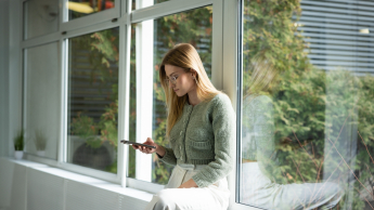 Zarządzanie nieruchomościami i homestaging | Studia II stopnia ze studiami podyplomowymi  | Uniwersytet WSB Merito w Gdańsku: Dziewczyna opiera się o parapet i przegląda telefon