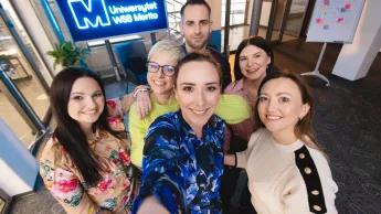 Indywidualne wsparcie, cyfrowe innowacje i inkluzyjne podejście – nowoczesny pracownik Publicznych Służb Zatrudnienia | Studia podyplomowe w Gdańsku | Uniwersytet WSB Merito w Gdańsku: Selfie słuchaczy studiów podyplomowych przy neonowym sygnecie Merito