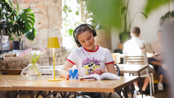 Bezpieczeństwo i przetrwanie w warunkach ekstremalnych | Studia I stopnia w Gdańsku | Uniwersytet WSB Merito w Gdańsku: Studentka w słuchawkach siedzi w kawiarni przy książce