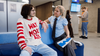 Dwójka studentów siedzi na kanapie przed Biurem Obsługi Studenta